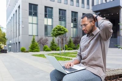 Young businesswoman using laptop while sitting on footpath in city