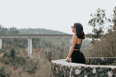 Side view of young woman sitting on retaining wall