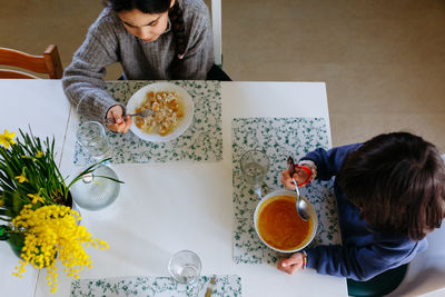 Upper view of two siblings eating lunch at home at white table with yellow flowers