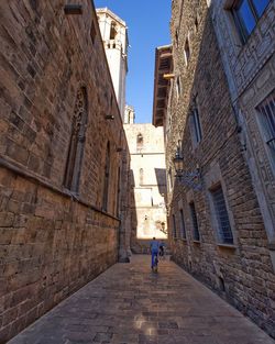 Rear view of man walking on alley amidst buildings in city