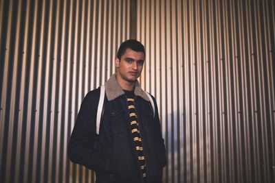 Portrait of young man with hands in pockets standing against wall