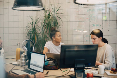 Multi-ethnic female hackers working at desk in creative office seen through window