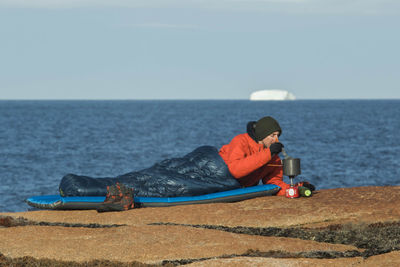 Man lying down on shore against sea against clear sky