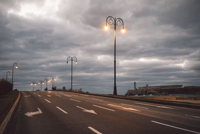 Street lights on road against cloudy sky
