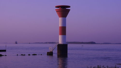 Lighthouse by sea against clear sky