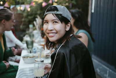 Portrait of smiling young woman wearing cap and sitting with friends at party in back yard