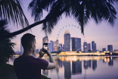 Man photographing by cityscape against sky during sunset
