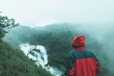 Rear view of person standing on landscape during rainy season