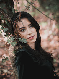 Close-up portrait of young woman standing against tree trunk