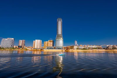 Buildings by river against clear blue sky