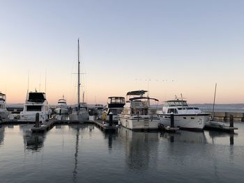 Boats moored in harbor at sunset