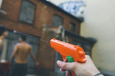 Cropped hand holding orange water gun by building