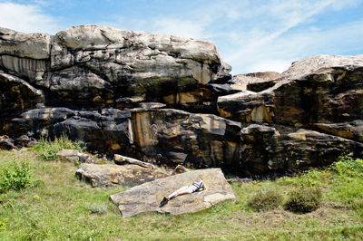 Woman lying on rock against sky during sunny day