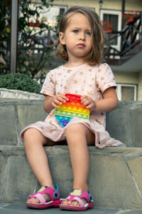 Portrait of concentrated cute little girl playing popit toy outdoors, in the yard of guest house.