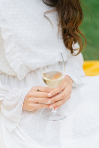 A glass of white wine or champagne in the hands of a young woman in a white dress. close-up