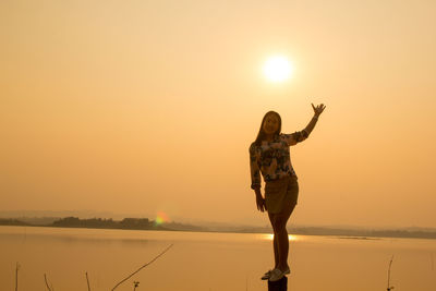 Portrait of woman standing on post against sea and sky during sunset