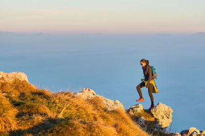 Person on rock by sea against sky during sunset