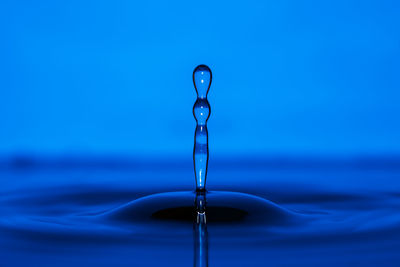 Close-up of drop falling on water against blue background