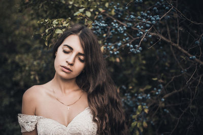 Portrait of young woman standing against tree