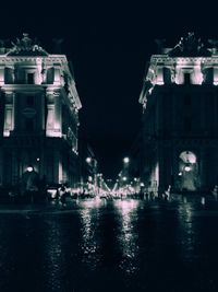 Illuminated buildings by street against sky at night