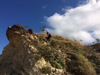 Low angle view of woman climbing on mountain against sky