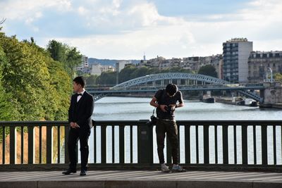 Men standing on bridge over river in city against sky