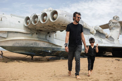 Family boy and his father in rocker clothes stand an abandoned ekranoplan plane by sea in dagestan