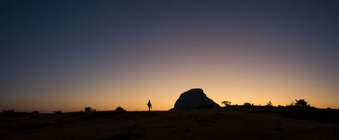 Silhouette rocks on land against sky during sunset