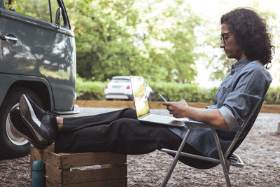 Side view of man using smart phone while sitting on chair during vacation