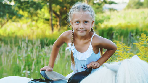 Blond girl of seven years, in a white dress, climbs, sits on a pony. cheerful, happy family