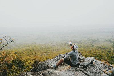 High angle view of male hiker pouring water on face while sitting on cliff