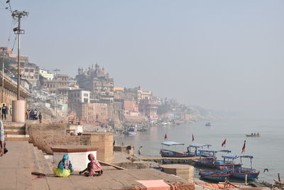 Boats in harbor by city against clear sky