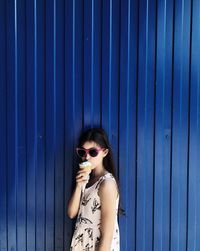 Woman wearing sunglasses standing against blue wall