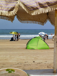 Green tent on the beach with few people walking around