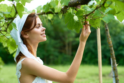 Side view of young woman standing by plants