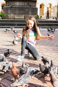 Girl feeding pigeons on city street