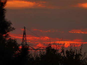 Low angle view of silhouette electricity pylon against dramatic sky