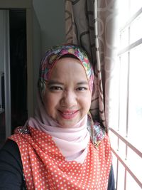 Portrait of smiling woman in hijab by window at home