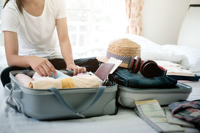 Midsection of woman packing luggage while sitting on bed at home