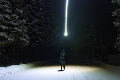 Rear view of woman standing on illuminated street at night