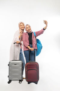 Smiling female friends taking selfie against white background