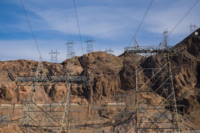 Electricity pylon by rock formation against sky