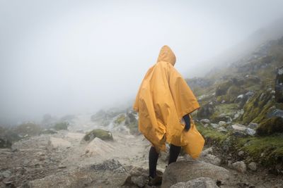 Man wearing raincoat while walking on landscape against sky