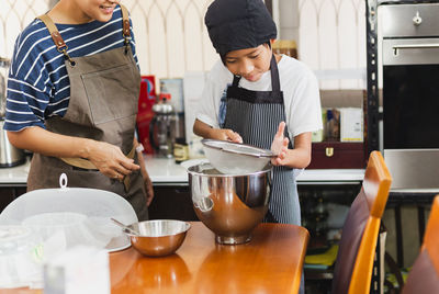 Mother and son sieving flour into a bowl for baking in kitchen