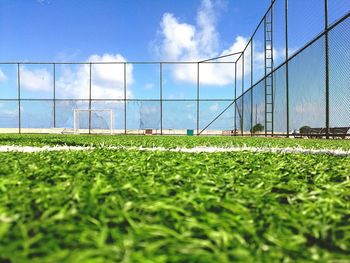 Surface level shot of soccer field by fence against sky