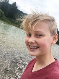 Portrait of boy with braces smiling at riverbank