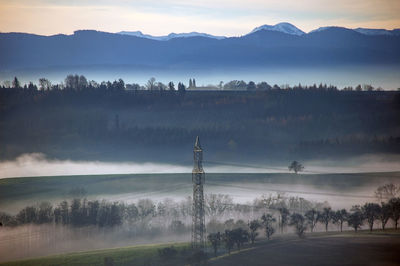 Electricity pylon on field against sky during foggy weather