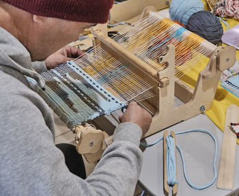 Man weaving small rug with pattern on wooden manual table loom.