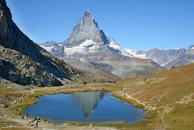 Scenic view of lake and rocky mountains against clear blue sky