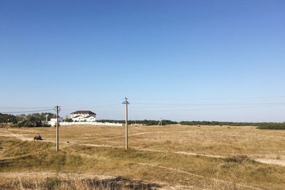 Telephone poles on field against clear blue sky